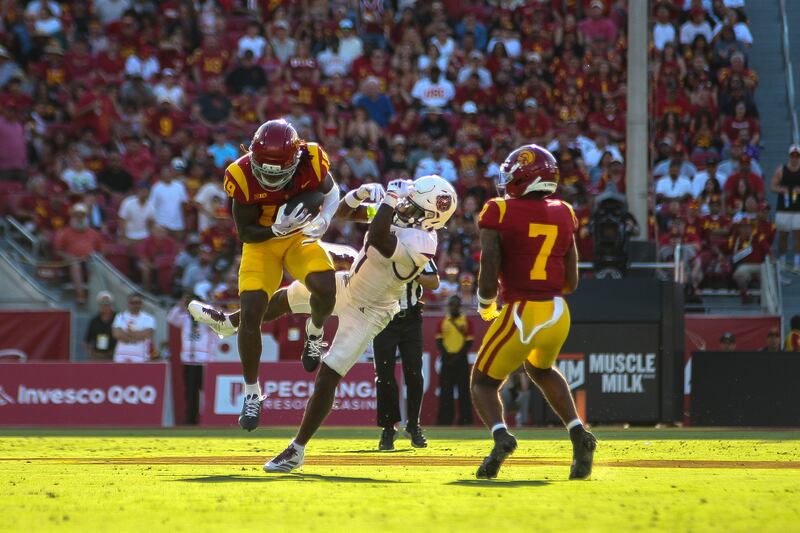Bishop Fitzgerald (19) leaps through the air to intercept a football intended for a Missouri State receiver as Kamari Ramsey (7) watches. Both Fitzgerald and Ramsey wear cardinal and gold football uniforms. The Missouri State receiver falls away and wears a white football uniform.