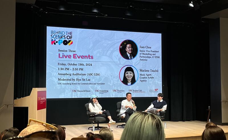 Photo of three people sitting in front of a screen on a stage