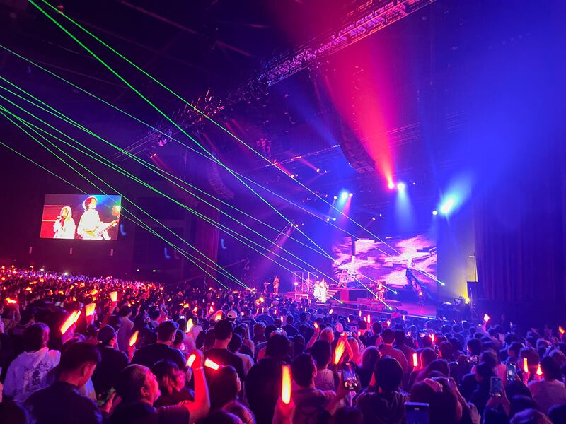 Photo of a crowd of people with red light sticks in front of a stage flashing green lights