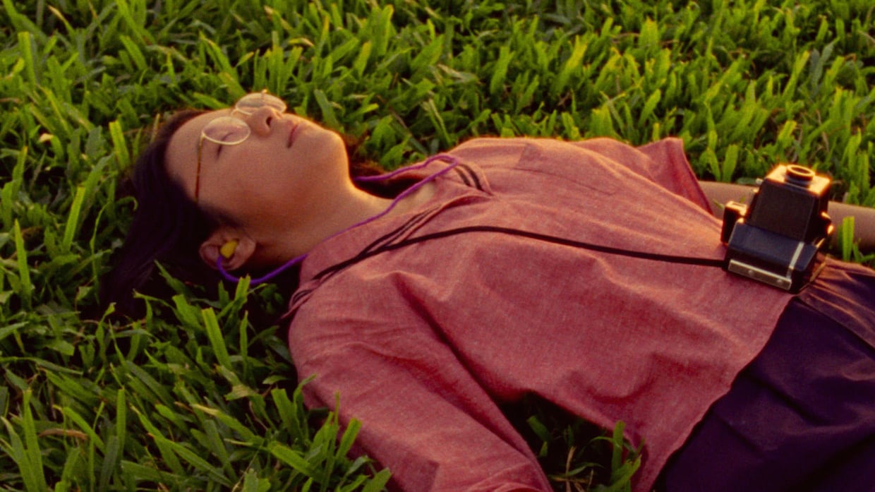 Girl lying down in the grass with a camera.