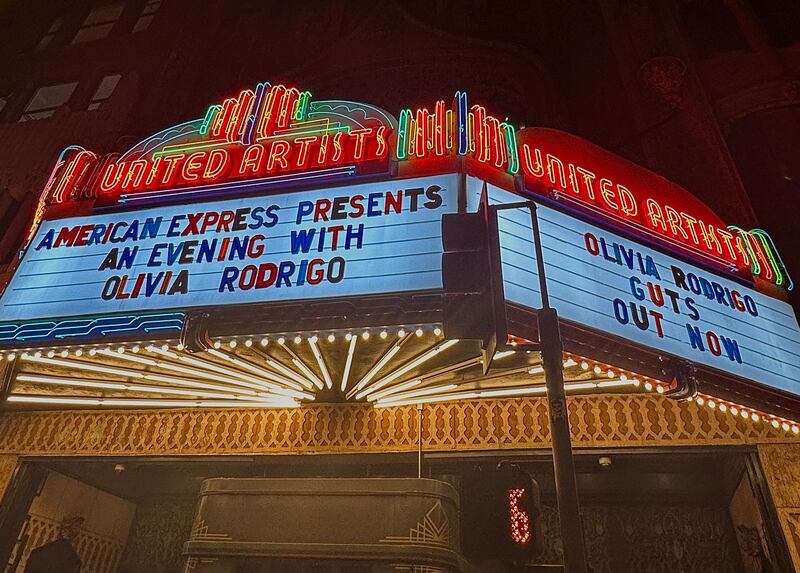 Glowing billboard outside of concert venue reads "American Express presents an evening with Olivia Rodrigo" and "Olivia Rodrigo GUTS out now."