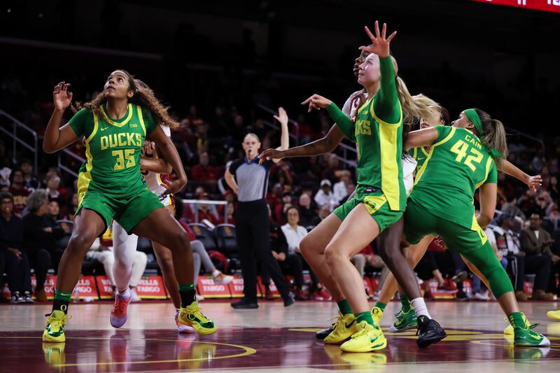 Oregon players box out in the lane at Galen Center. They wear green uniforms with yellow accents and shoes.