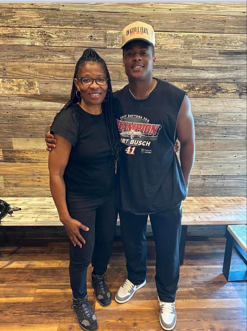 Brenda Smith stands on the left and Jared Smith stands on the right, smiling with their arms around each other. Both are dressed in black athletic clothing, standing in front of a wood-paneled wall with a bench behind them.