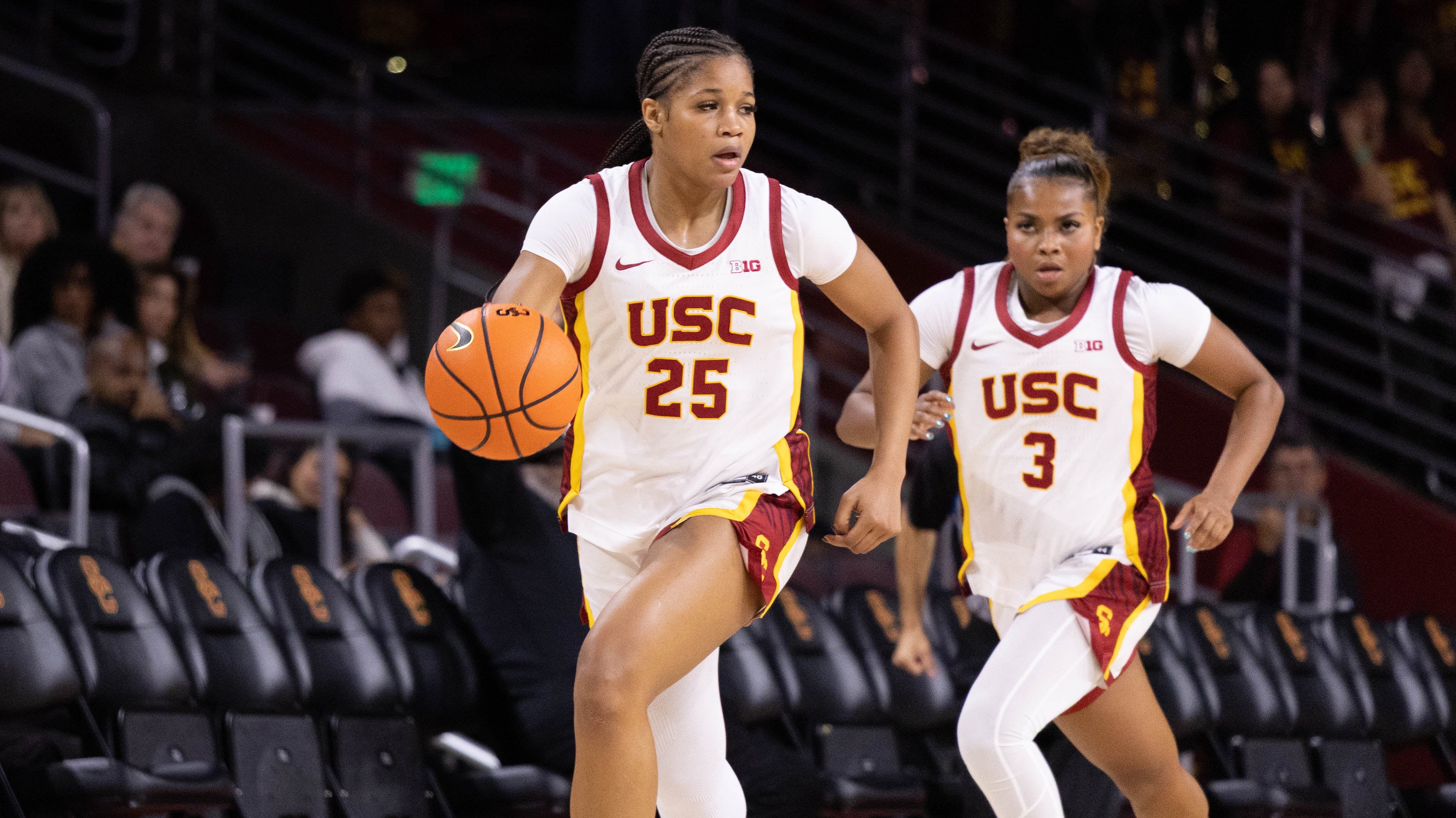 Photo of USC basketball player in white jersey dribbling.