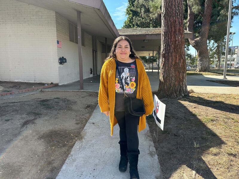 A woman in a yellow sweater standing outside of a building.