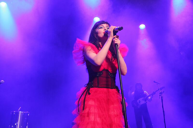 Photo of a woman with a microphone in front of a purple backdrop