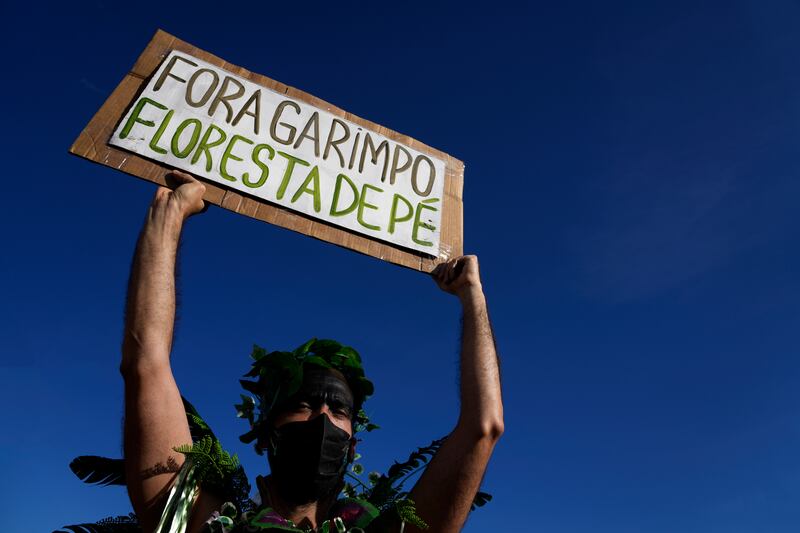 Photo of a protestor holding up a sign made of cardboard and white paper in Portuguese that reads 'Mining out. The forest stands.'