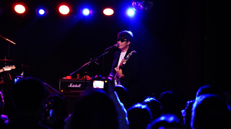 Photo of a man with a guitar and sunglasses in front of a crowd