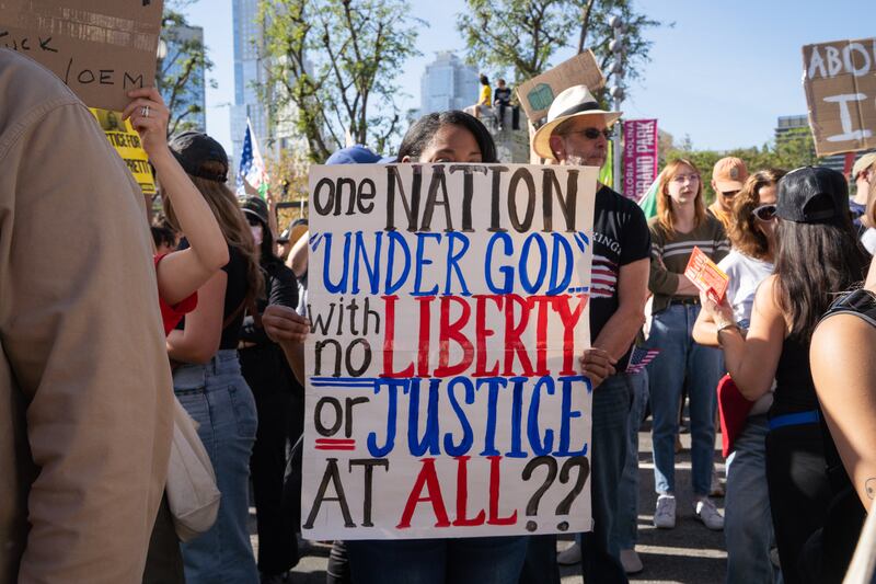 A protester holds a sign reading "one nation 'under god' with no liberty or justice at all??"