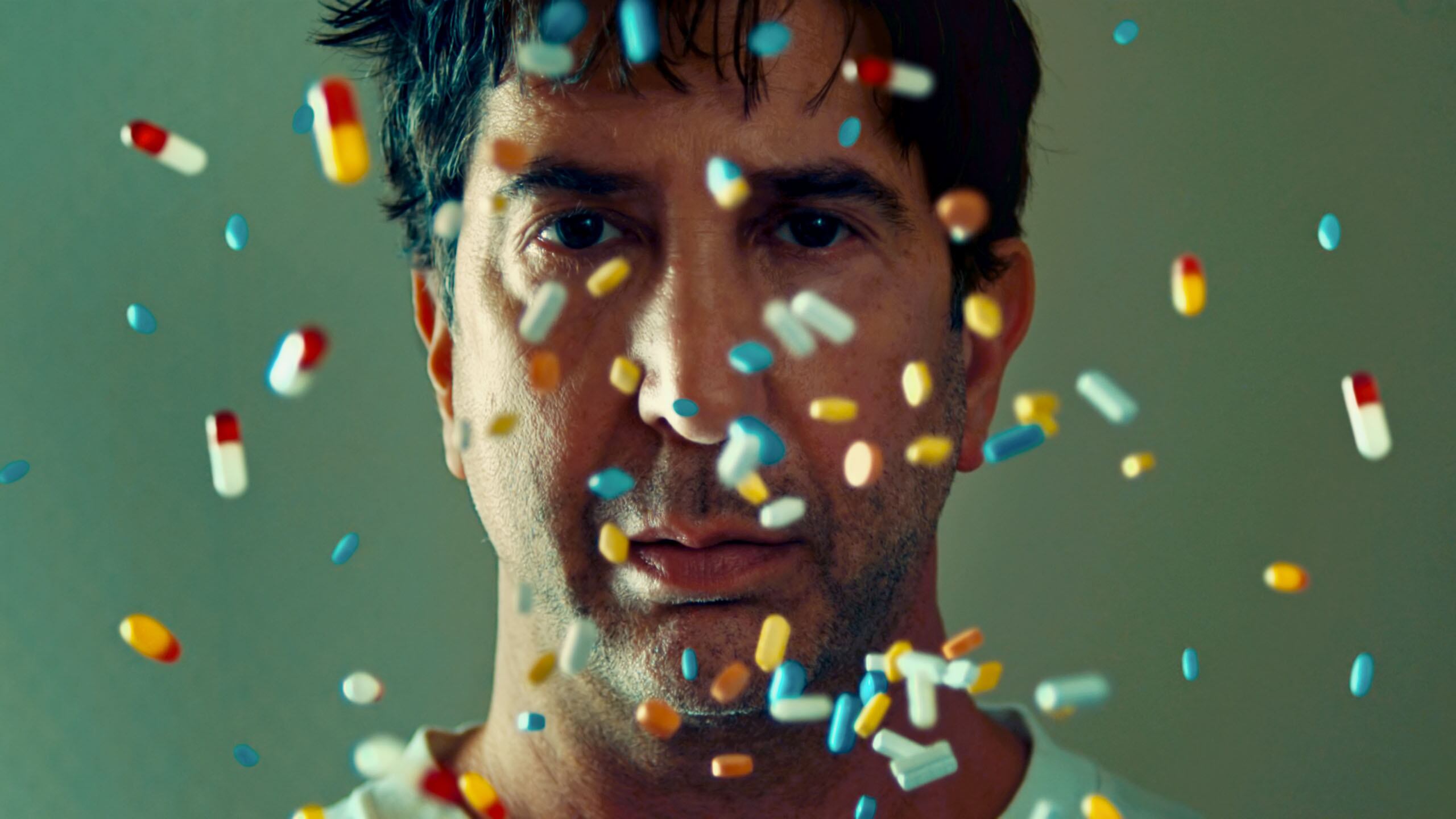 A photo of David Schwimmer with dozens of multicolored pills in front of his face.
