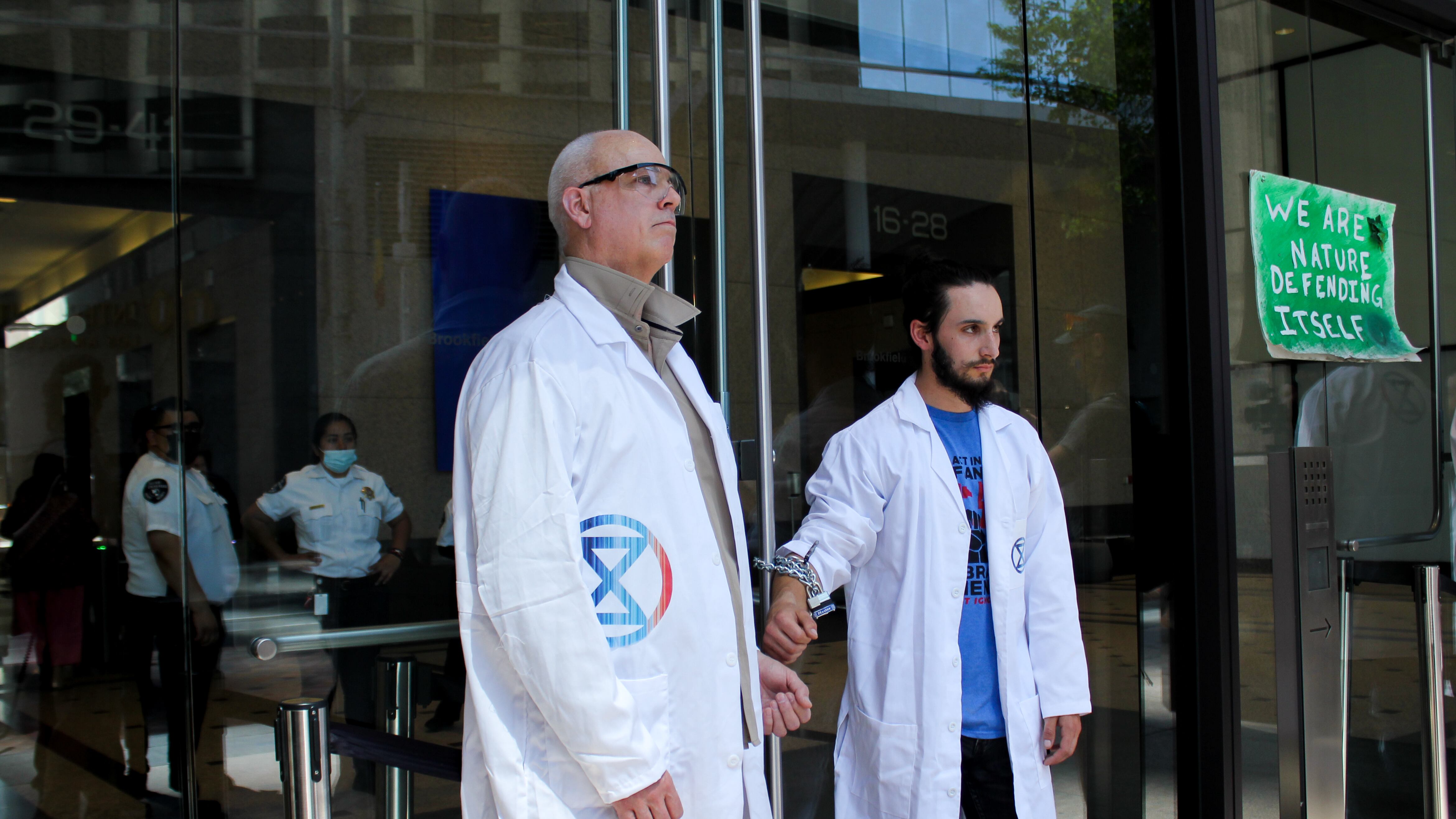 Two men stand with their wrists chained to the front doors of a Chase bank as security watches.
