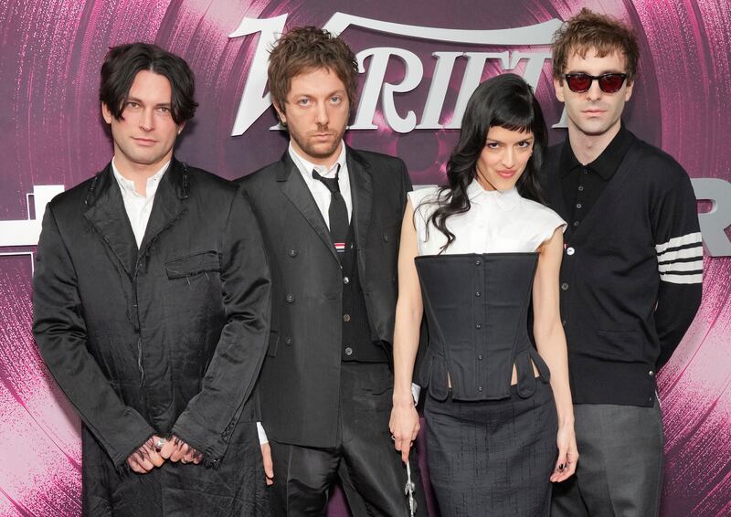 Photo of three men and a woman posing for pictures in front of a purple background.