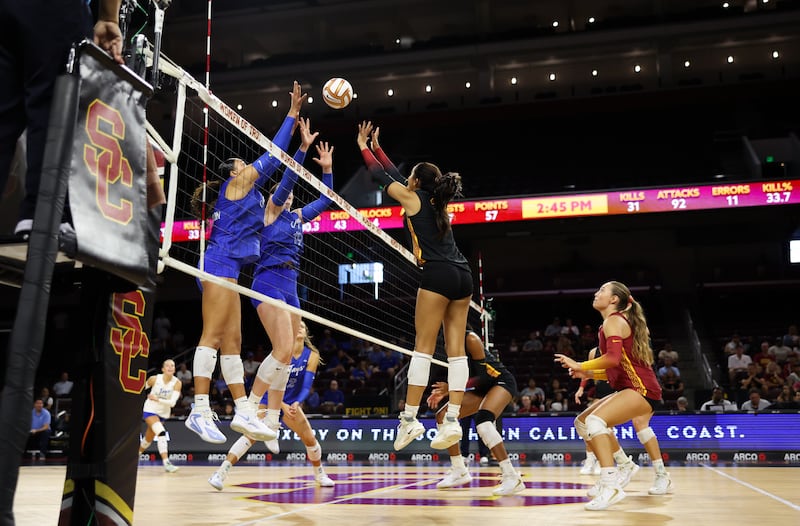 London Wijay jumps above the net in a head-to-head battle with two Creighton players on the other side of the net.