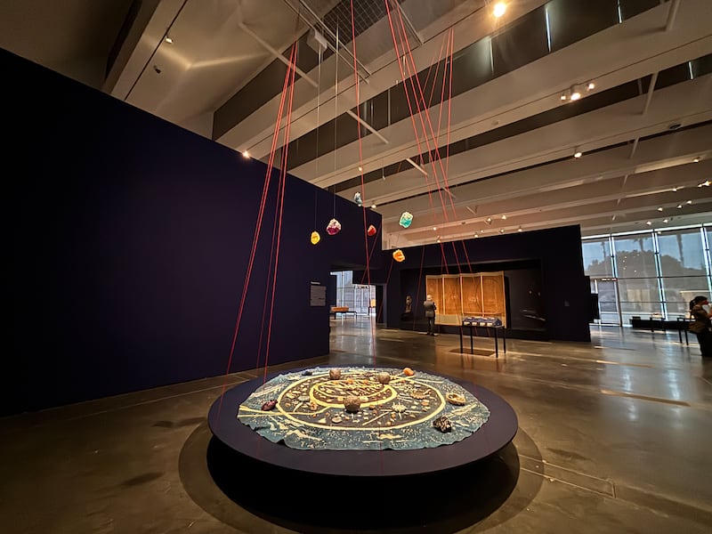 A round canvas painted with acrylic and decorated with concrete bowls, shells and salt crystals. Above the canvas, planet-like star stones float suspended in the air by yarn.