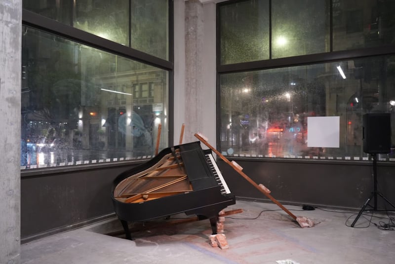A grand piano is deconstructed and slanted on the ground. The top of the piano is taken off, as well as the legs.