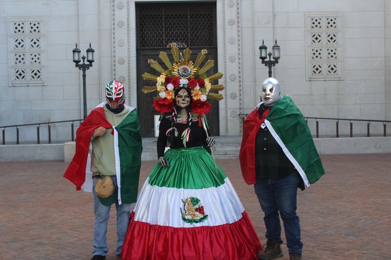 Photo of two people dressed as luchadores and a one person dressed as a catrina between them.
