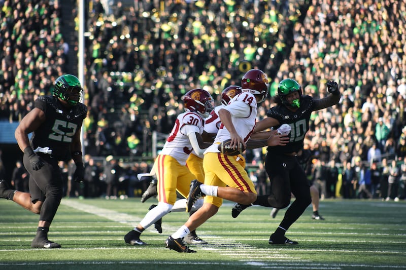 Jayden Maiava (14) runs with football in hand. Trojan blockers and Oregon defenders can be seen in the background.