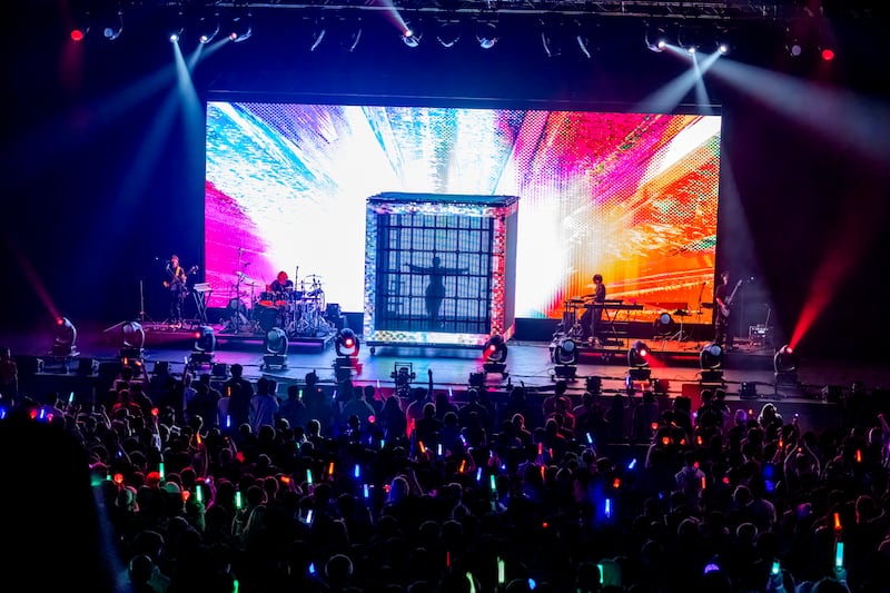 Photo of a stage with a cage at the center with a woman inside and a multi-colored background