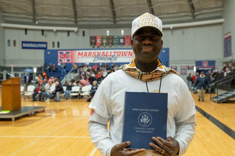 Austin Craig holds a blue caucus captain notebook and wears a white hat that reads "Trump Caucus Captain."