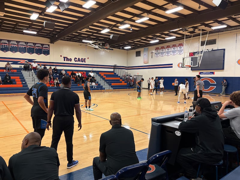 A coach and a player discuss strategy while another player shoots a free throw.