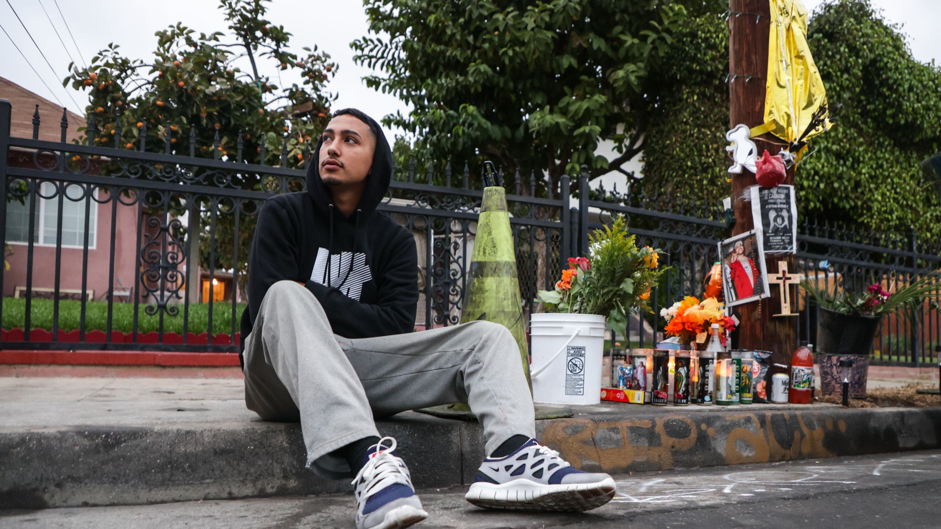 A photo of a man sitting at the memorial site for Efrain Moreno with candles and photos.