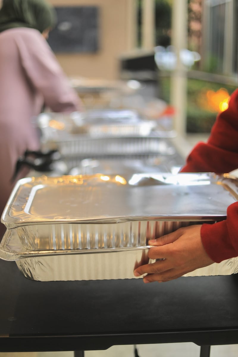 Person holding a silver aluminum food tray.