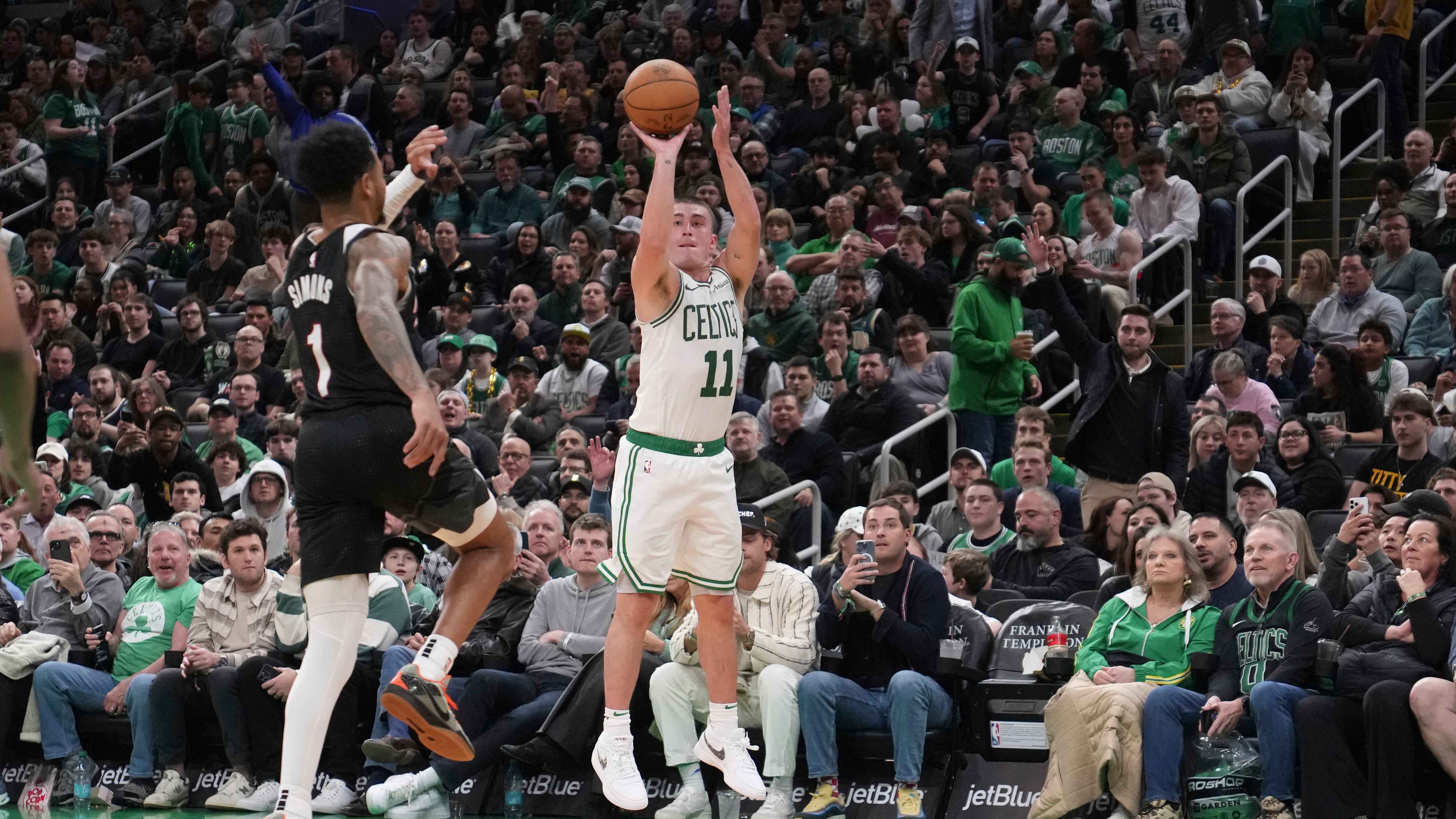 Boston Celtics guard Payton Pritchard (wearing number 11 in white and green) takes a 3-pointer during a game against the Portland Trail Blazers on Wednesday, March 5. Blazers guard Anfernee Simons (wearing number 1 in black and red) tries to leap out and contest the shot.