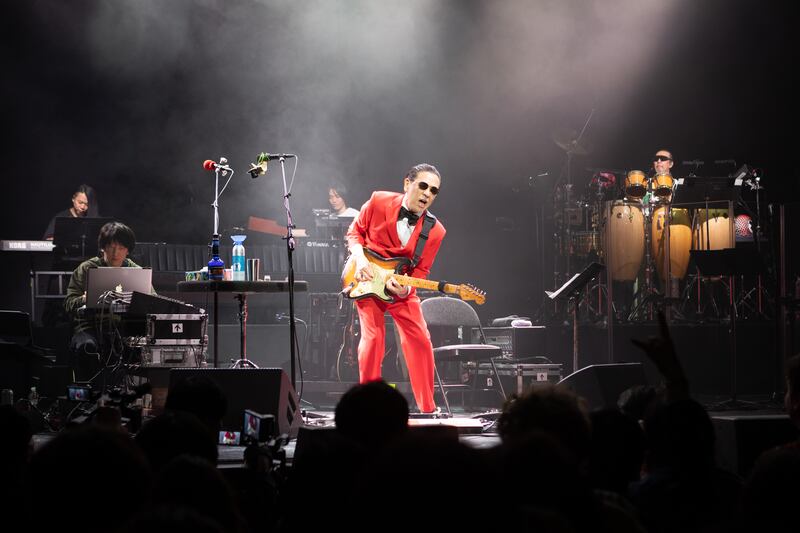 Photo of a man in a red suit and bowtie playing the guitar on stage