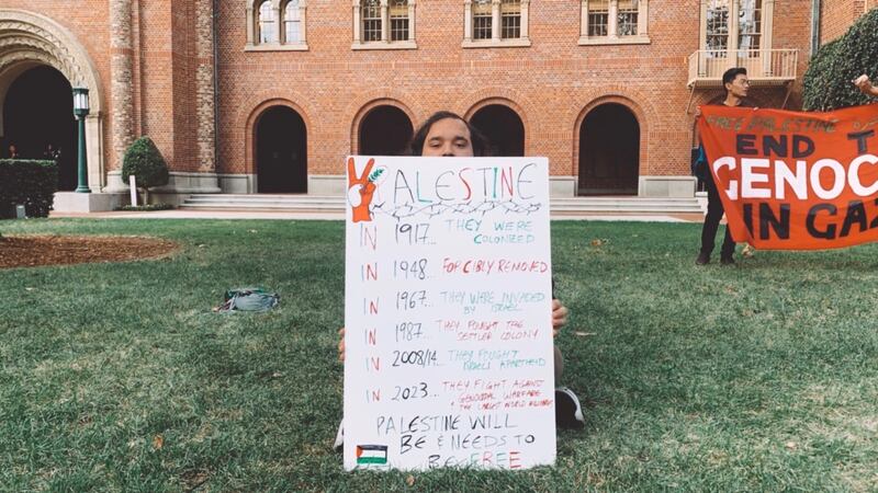 A protester holds a sign listing a brief collection of Palestine’s history from 1917 to the present.