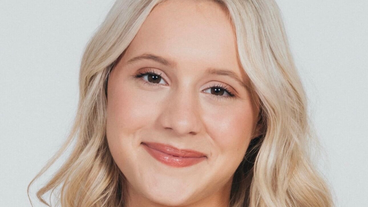 Kameron smiles at the camera in a headshot with a white background. She has blonde hair and is wearing a black top.