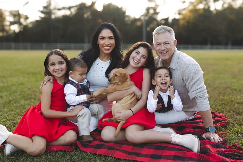 Photo of a family, two adults, two young girls, two young boys, and their dog posed in a park.