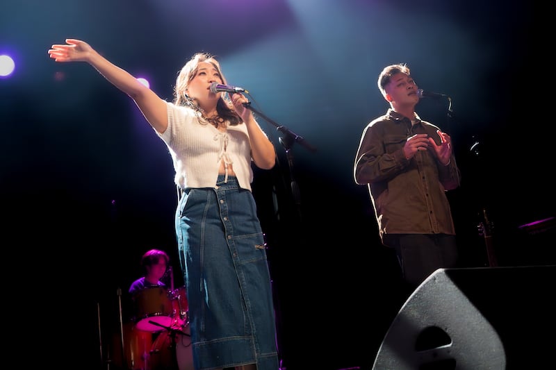 Kang waves her right hand at the crowd from the stage, as Orion Song sings emotionally by her side.