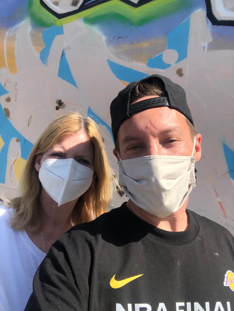 Michael and his mother stand in front of a spray-painted wall with masks on