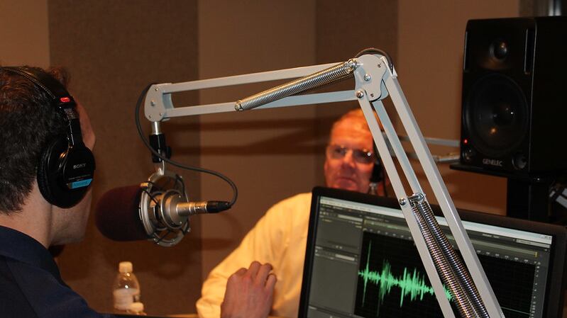 Photo of two men in a studio speaking into a microphone