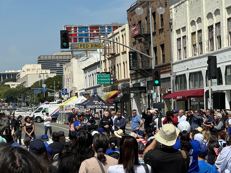 A crowd stands around a man in a blue Dodgers shirt holding a megaphone